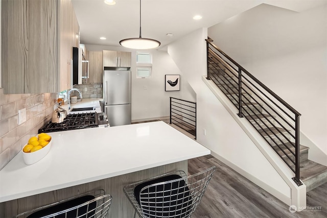 kitchen featuring backsplash, kitchen peninsula, hanging light fixtures, stainless steel appliances, and light brown cabinetry