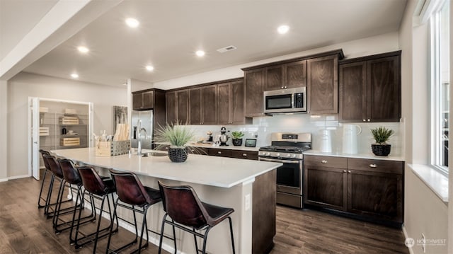 kitchen featuring dark brown cabinetry, dark hardwood / wood-style floors, appliances with stainless steel finishes, and a center island with sink