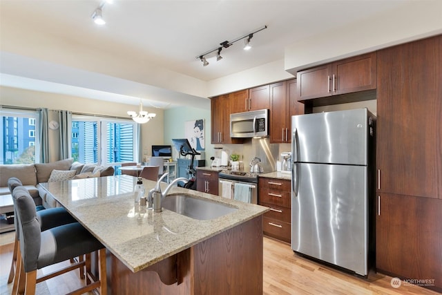 kitchen with a breakfast bar, sink, a kitchen island with sink, light stone countertops, and appliances with stainless steel finishes