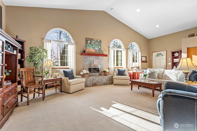 living room with light carpet, a healthy amount of sunlight, a tiled fireplace, and high vaulted ceiling