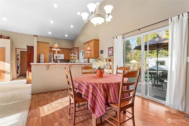 dining space featuring high vaulted ceiling, light wood-type flooring, and an inviting chandelier