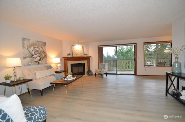 living room with baseboards, a tile fireplace, a textured ceiling, and light wood-style floors