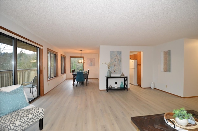 living room featuring baseboards, an inviting chandelier, a textured ceiling, and light wood-style floors