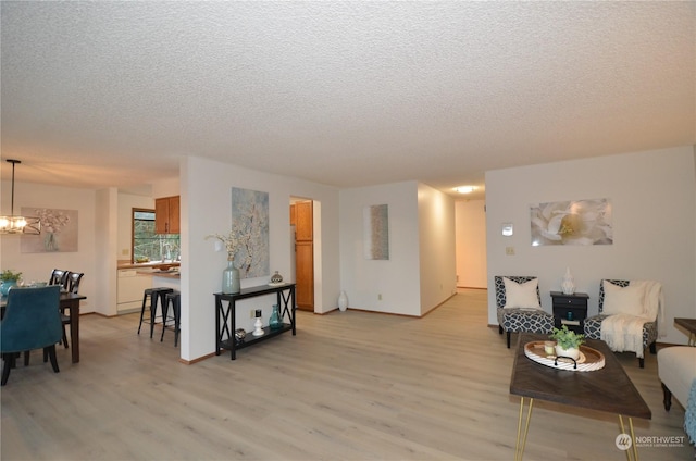 living room with a textured ceiling, light wood finished floors, baseboards, and an inviting chandelier