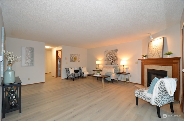 living room featuring light wood-type flooring, baseboards, a textured ceiling, and a tiled fireplace