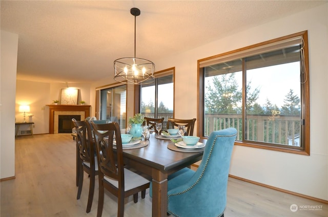 dining space with a textured ceiling, light wood finished floors, baseboards, a chandelier, and a tile fireplace