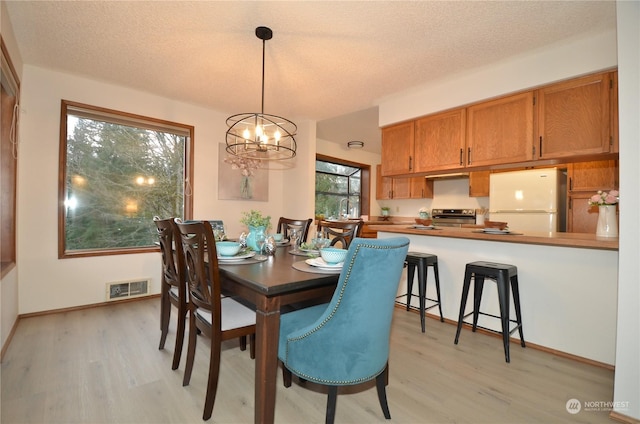 dining area with a textured ceiling, baseboards, visible vents, and light wood-style floors