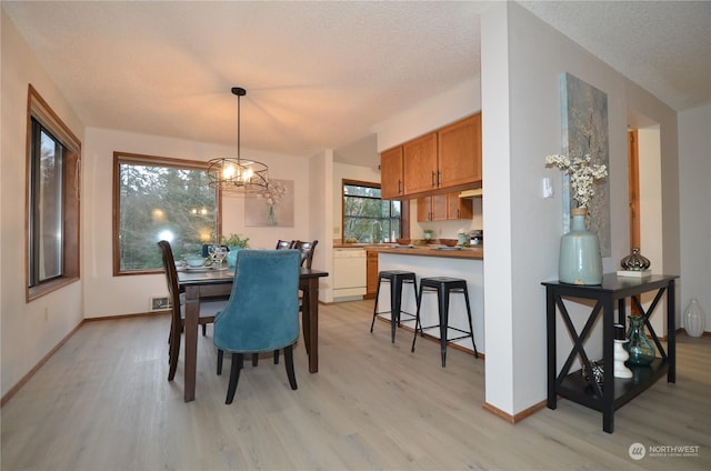 dining space with light wood-style flooring, a textured ceiling, and baseboards