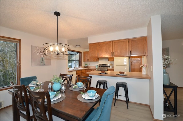 dining space with light wood-style flooring, a notable chandelier, visible vents, and a textured ceiling