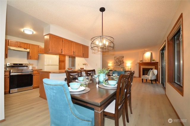 dining room featuring light wood-style floors, a chandelier, a fireplace, and a textured ceiling