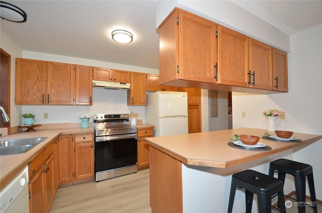 kitchen with white appliances, a peninsula, light countertops, under cabinet range hood, and a sink