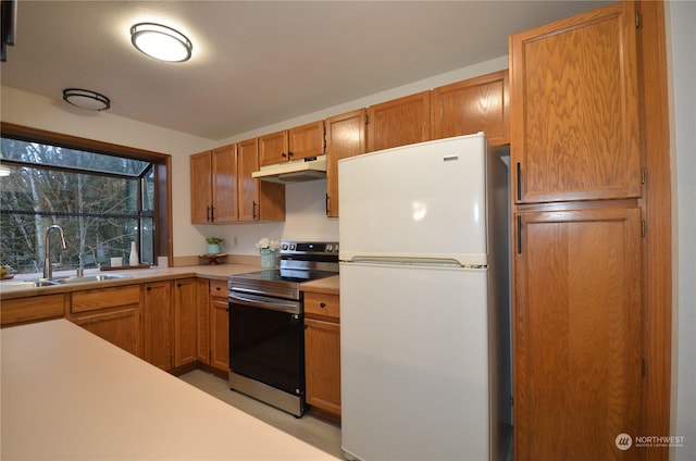 kitchen with stainless steel electric stove, light countertops, freestanding refrigerator, a sink, and under cabinet range hood