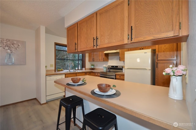 kitchen with light wood-type flooring, a textured ceiling, white appliances, a peninsula, and light countertops