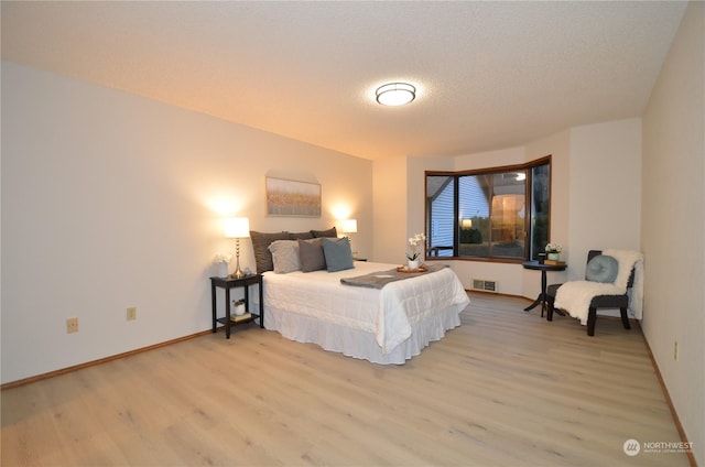 bedroom featuring visible vents, light wood-style flooring, baseboards, and a textured ceiling