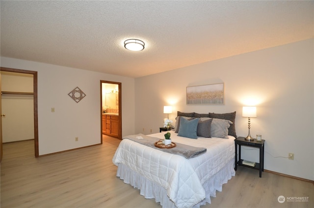 bedroom featuring a textured ceiling, baseboards, light wood-style floors, a walk in closet, and ensuite bath