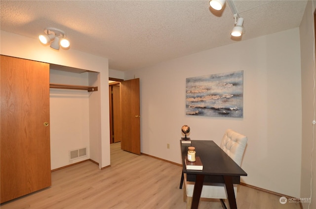 office with light wood finished floors, baseboards, visible vents, and a textured ceiling