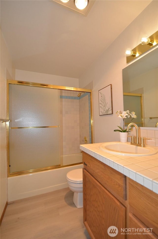 full bathroom featuring toilet, bath / shower combo with glass door, wood finished floors, and vanity