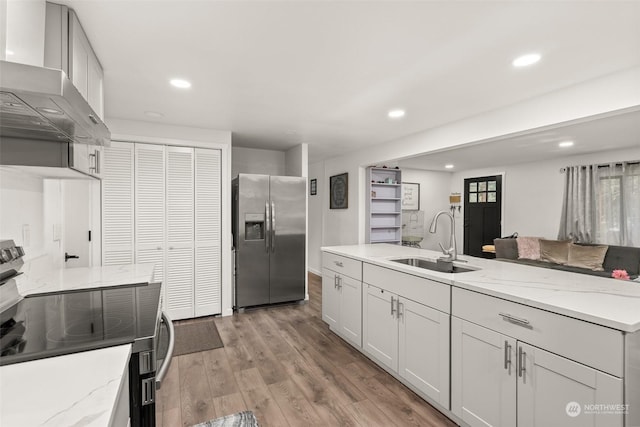 kitchen featuring appliances with stainless steel finishes, light wood-type flooring, wall chimney range hood, white cabinets, and sink