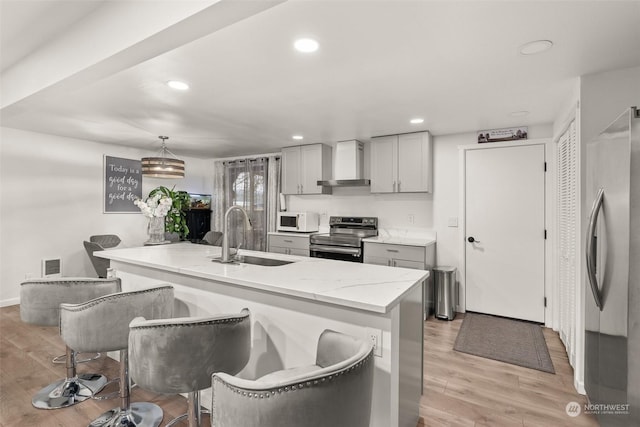 kitchen featuring appliances with stainless steel finishes, a kitchen island with sink, wall chimney range hood, pendant lighting, and sink