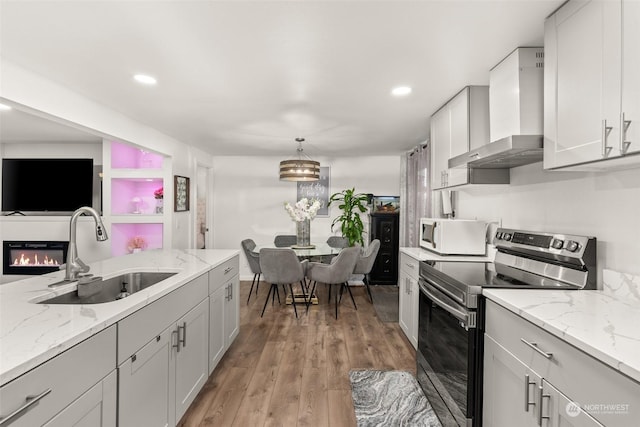 kitchen featuring stainless steel range with electric cooktop, decorative light fixtures, wall chimney range hood, light hardwood / wood-style flooring, and sink