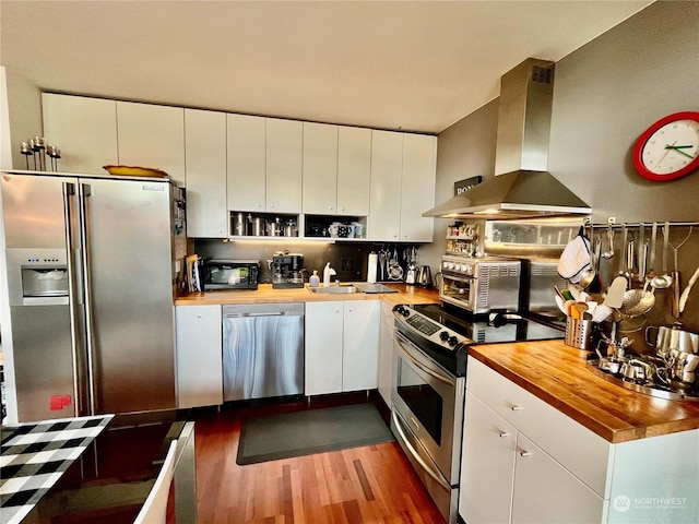 kitchen featuring butcher block counters, island exhaust hood, stainless steel appliances, and white cabinetry