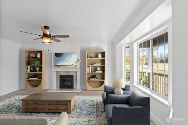 living room with hardwood / wood-style flooring, ceiling fan, ornamental molding, and a tile fireplace