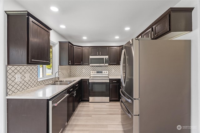 kitchen with dark brown cabinetry, sink, tasteful backsplash, light wood-type flooring, and appliances with stainless steel finishes