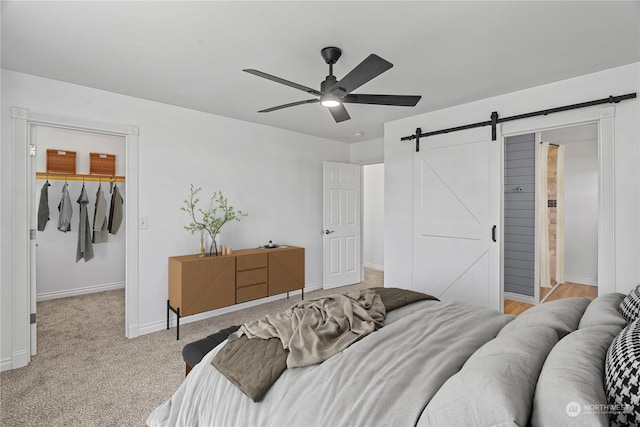 bedroom featuring a walk in closet, light carpet, a closet, ceiling fan, and a barn door