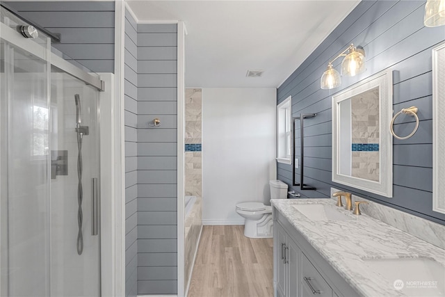 full bathroom featuring toilet, wood walls, wood-type flooring, shower with separate bathtub, and vanity