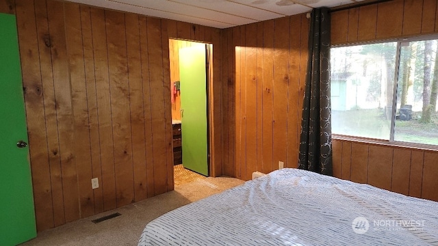 bedroom featuring multiple windows, wooden walls, and light carpet