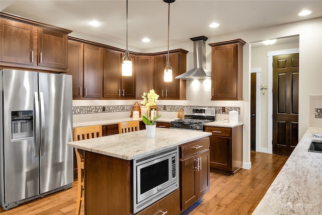 kitchen with decorative light fixtures, decorative backsplash, light stone counters, stainless steel appliances, and wall chimney range hood