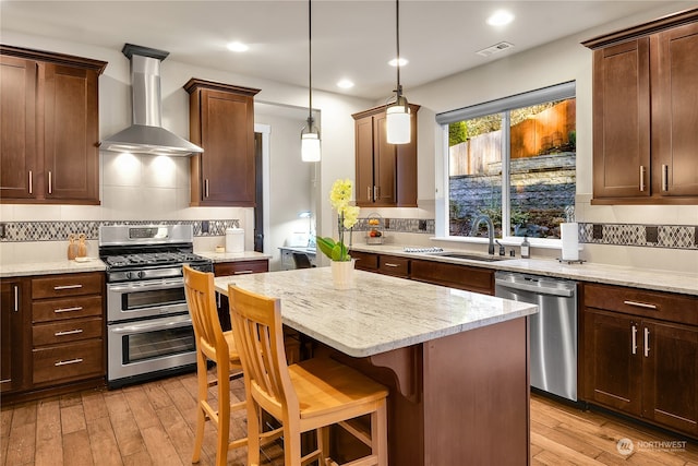 kitchen with a kitchen bar, sink, appliances with stainless steel finishes, pendant lighting, and wall chimney range hood