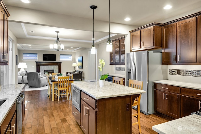 kitchen with appliances with stainless steel finishes, a kitchen breakfast bar, a raised ceiling, hardwood / wood-style flooring, and light stone countertops