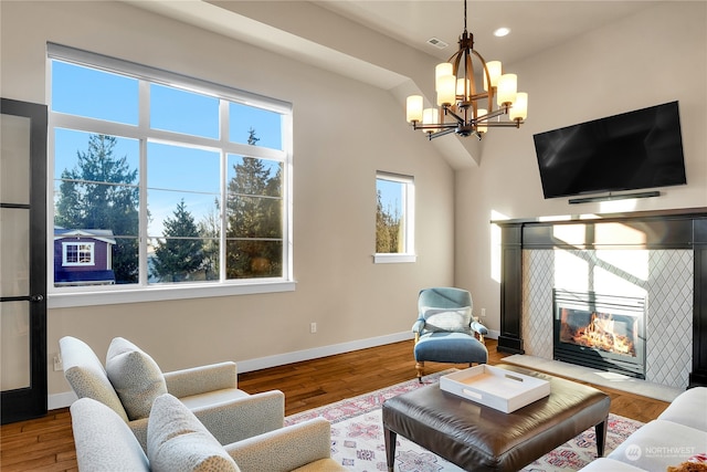 living room with hardwood / wood-style flooring, a tiled fireplace, and an inviting chandelier