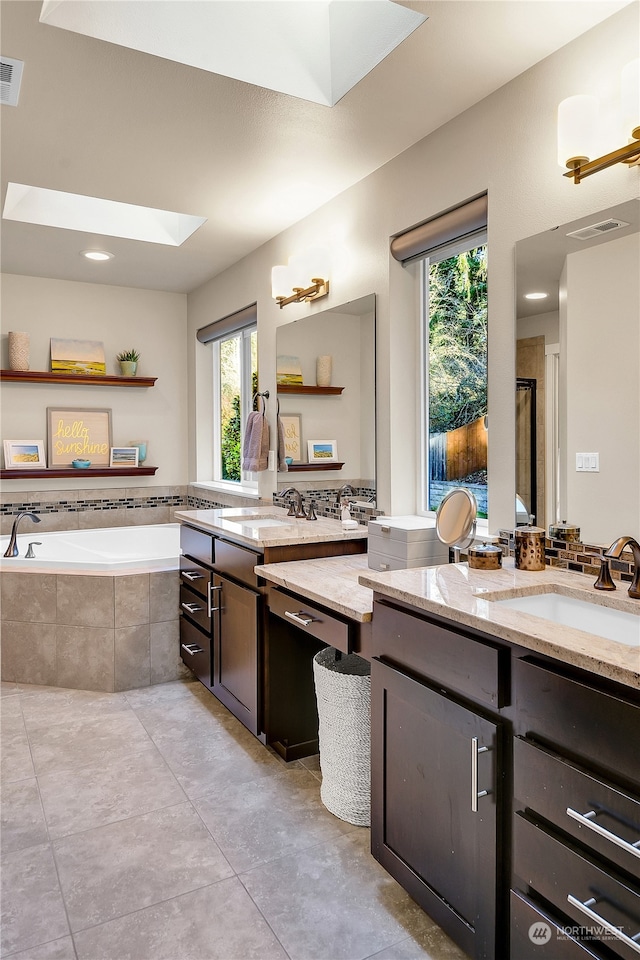 bathroom featuring tile patterned flooring, a skylight, vanity, tiled bath, and decorative backsplash