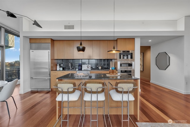 kitchen featuring decorative backsplash, dark hardwood / wood-style floors, decorative light fixtures, dark stone counters, and stainless steel built in refrigerator