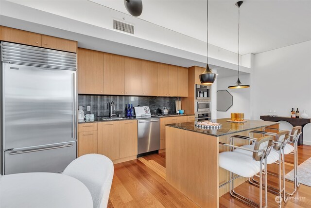 kitchen with light brown cabinets, built in appliances, sink, backsplash, and hanging light fixtures