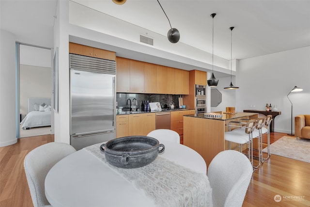 kitchen featuring stainless steel appliances, decorative backsplash, light wood-type flooring, hanging light fixtures, and sink