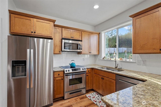 kitchen with light stone countertops, appliances with stainless steel finishes, light hardwood / wood-style floors, sink, and backsplash