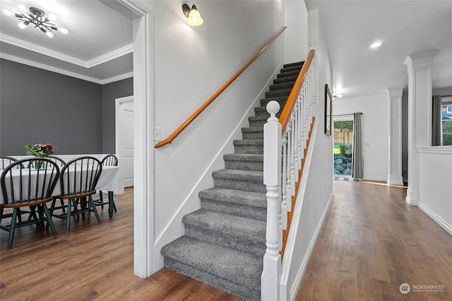 stairway featuring hardwood / wood-style floors, a notable chandelier, crown molding, and decorative columns