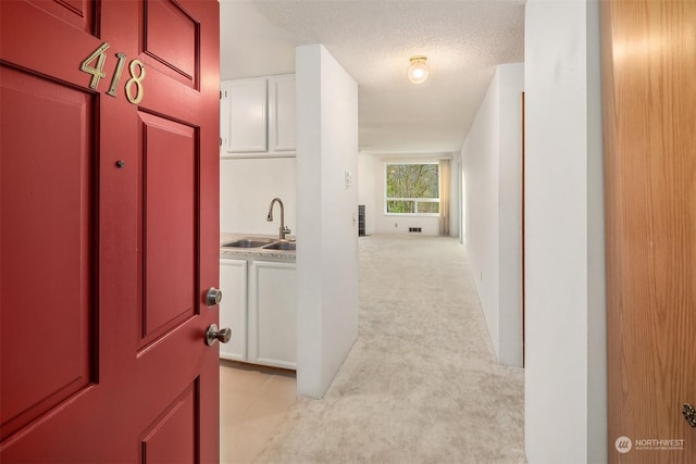 corridor with sink, light colored carpet, and a textured ceiling