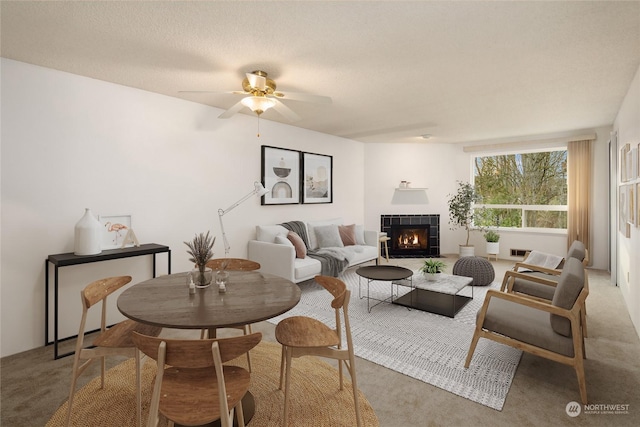 living room with ceiling fan, a fireplace, a textured ceiling, and carpet