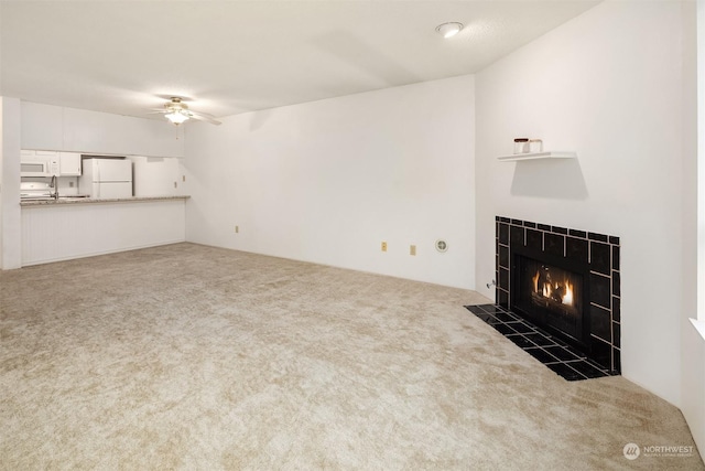 unfurnished living room featuring ceiling fan, sink, a tiled fireplace, and dark carpet