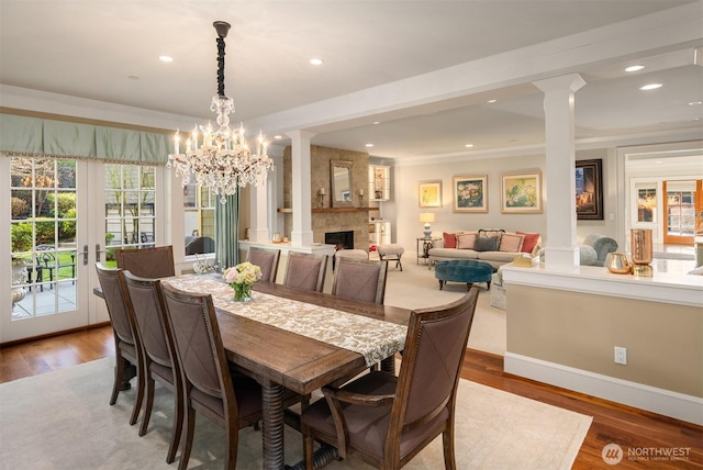 dining space featuring a fireplace, a notable chandelier, decorative columns, and wood finished floors