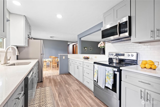 kitchen with stainless steel appliances, tasteful backsplash, light wood-type flooring, light stone counters, and sink