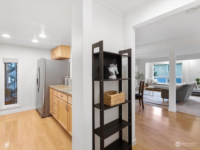 kitchen with light brown cabinetry, stainless steel refrigerator, ornamental molding, and light wood-type flooring