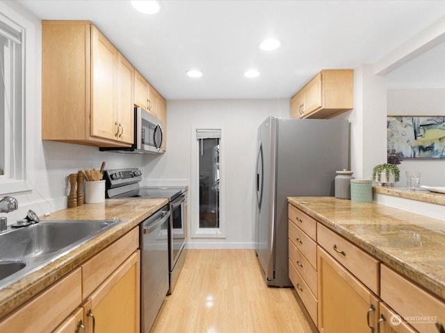 kitchen with stainless steel appliances, light brown cabinetry, light hardwood / wood-style floors, sink, and light stone counters