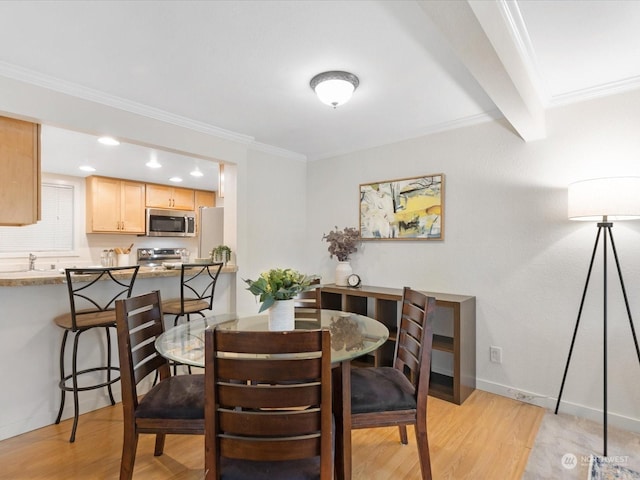 dining room with sink, light wood-type flooring, beamed ceiling, and ornamental molding