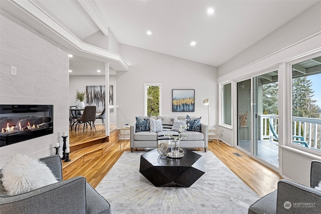 living room with a tile fireplace, vaulted ceiling with beams, and light wood-type flooring