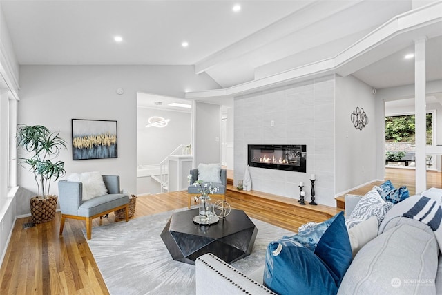 living room featuring a tiled fireplace, vaulted ceiling, and light hardwood / wood-style flooring